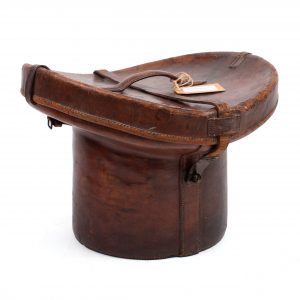 Brown leather hat box in cowhide in the shape of a top hat, lid with handle, buckles and interior in burgundy cloth.