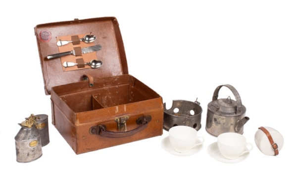 Late 19th century cardboard picnic basket manufactured by “SIRRAM”, includes a leather handle and metal spring closure. It contains a kettle, a burner signed by the manufacturer, a bottle for alcohol and a bottle of cream milk in zinc sheet with brass caps. Two sets of cup and plate, and sugar bowl in English ceramic. There are two spoons and a knife on the lid.