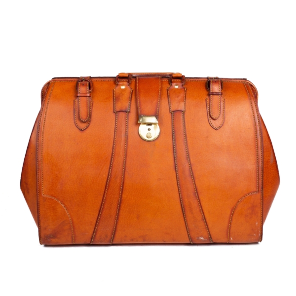 Honey pigskin travel suitcase, handle, two buckle closure straps and tab lock.